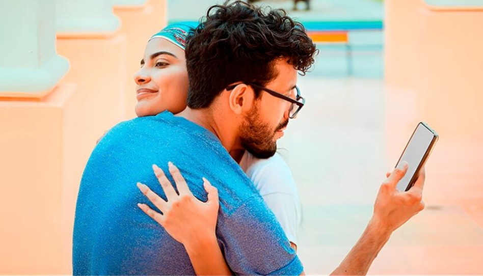 ఒక మహిళ తన భాగస్వామిని ఆత్మీయంగా కౌగిలించుకుని ఉండగా, ఆ పురుషుడు ఆమెను పక్కనబెట్టి దొంగతనంగా తన మొబైల్ స్క్రీన్ వైపు చూస్తున్న దృశ్యం.