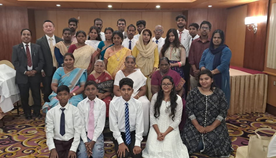 సమావేశ మందిరంలో సంప్రదాయ దుస్తులు మరియు ఫార్మల్ దుస్తులు ధరించి కలిసి నిలబడిన పుదుచ్చేరి కడవరి దిన పరిశుద్ధుల సంఘ సభ్యుల సమూహ చిత్రం.
